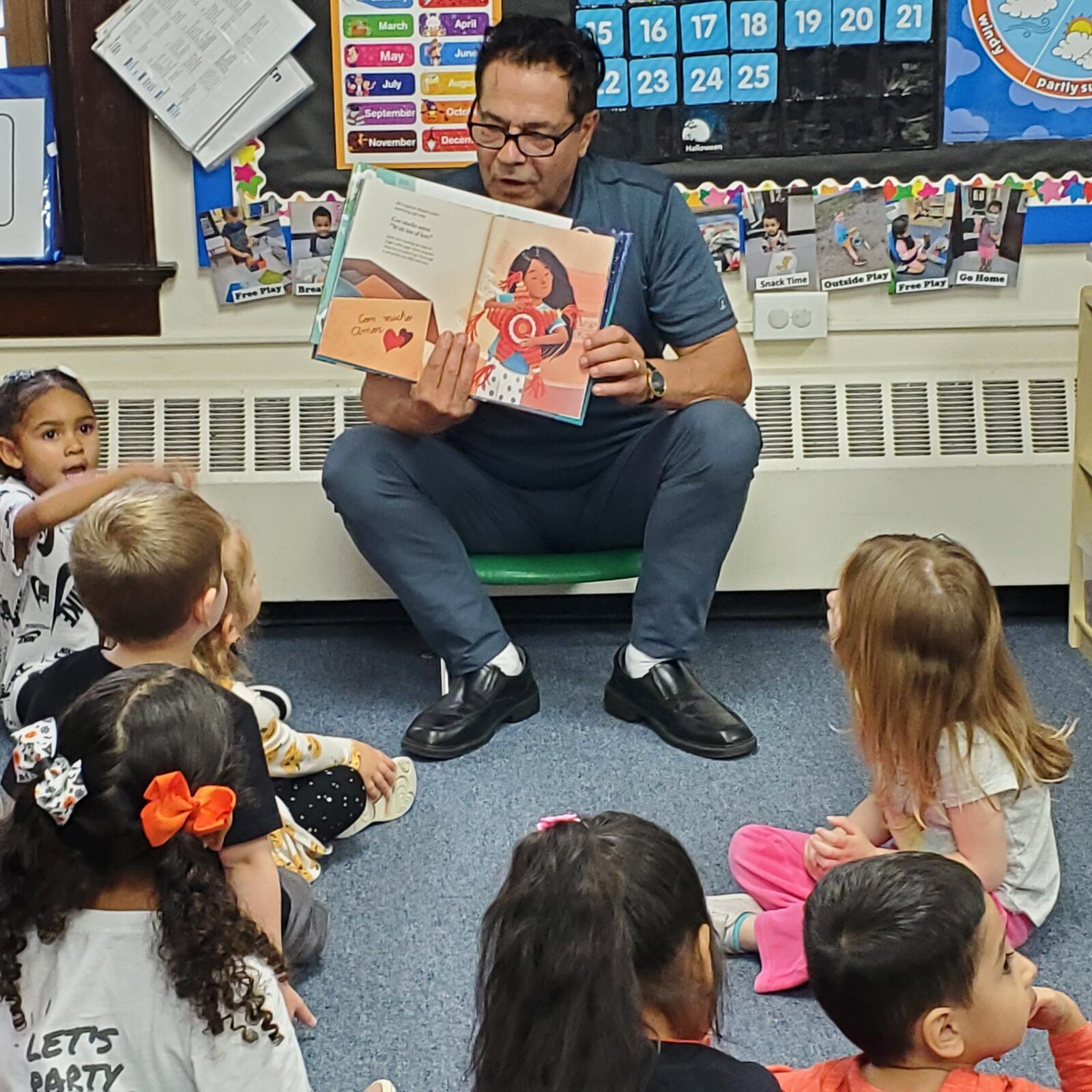 A visiting reader showing a picture book to children seated on the classroom floor