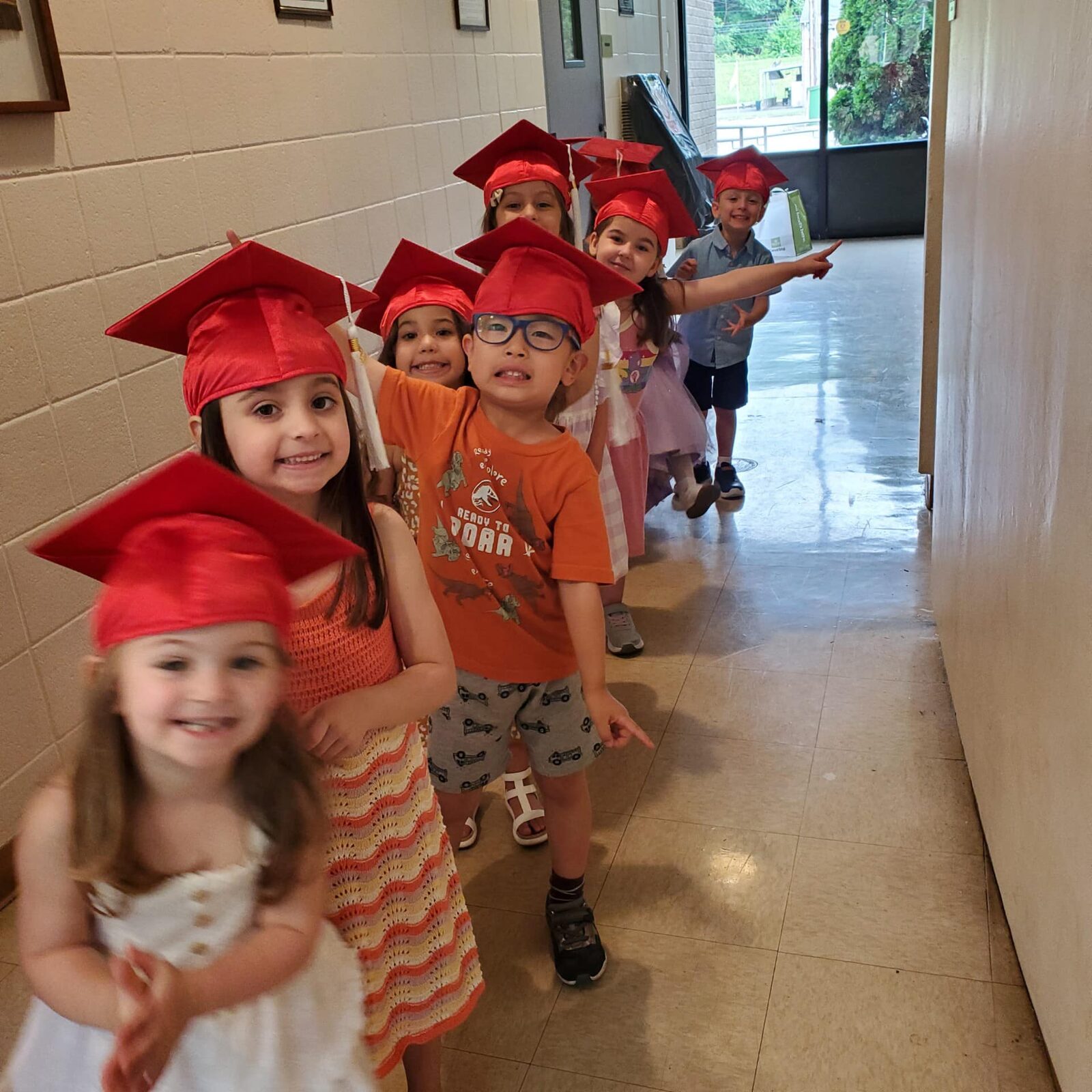 Graduating children wearing red mortarboard caps