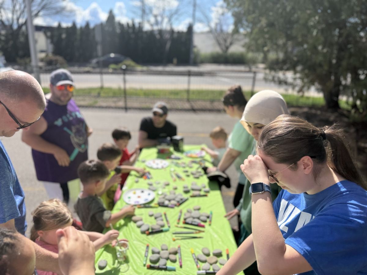 Families and children painting rocks together at a long outdoor table