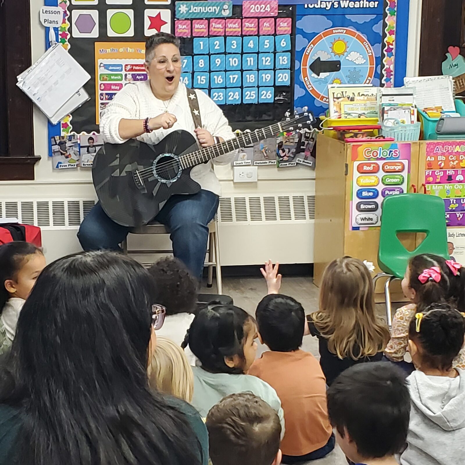 Children sitting in a circle during a music lesson with a guitar