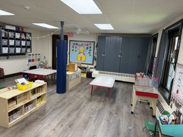 A classroom with cubby shelving, an art table, child-height furniture and a padded blue support column