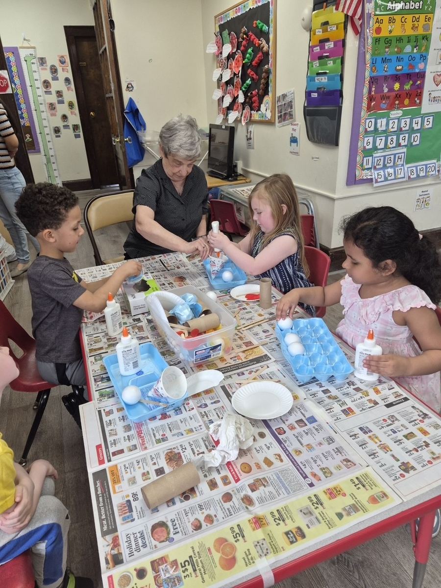 A senior center visitor doing a craft project with children at a classroom table