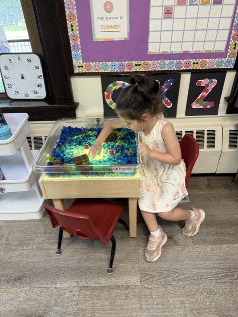 A child playing at a sensory table filled with blue and green material